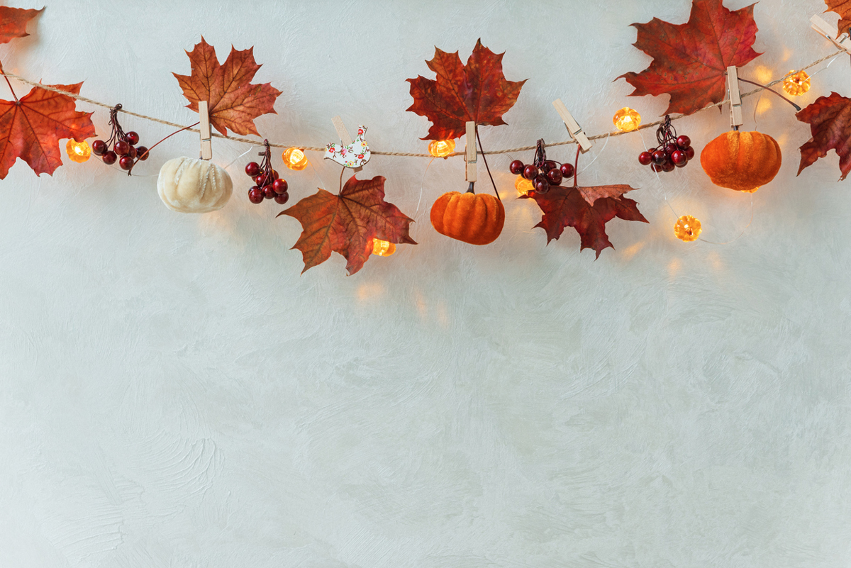 Ručně vyráběná podzimní dekorace z listů, malých dýní a světýlek zavěšená na provázku.