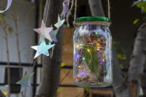 Závěsná dekorace ze zavařovací sklenice s drobnými světýlky, sušenými listy a provázkem.