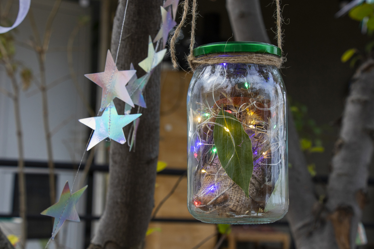 Závěsná dekorace ze zavařovací sklenice s drobnými světýlky, sušenými listy a provázkem.