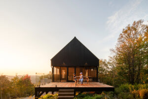 Moderní dům s černou fasádou a prostornou terasou s posezením při západu slunce.