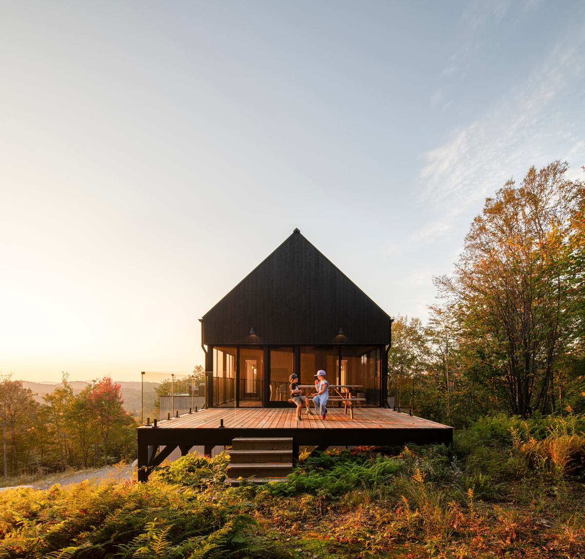 Moderní dům s černou fasádou a prostornou terasou s posezením při západu slunce.