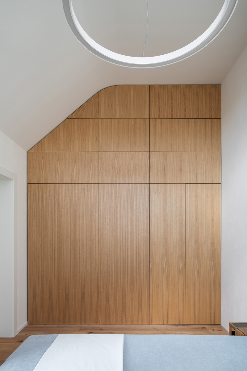 Vestavěné úložné skříně na míru v ložnici rekonstruovaného domu v Křenovicích, s dýhovaným obkladem až ke stropu.