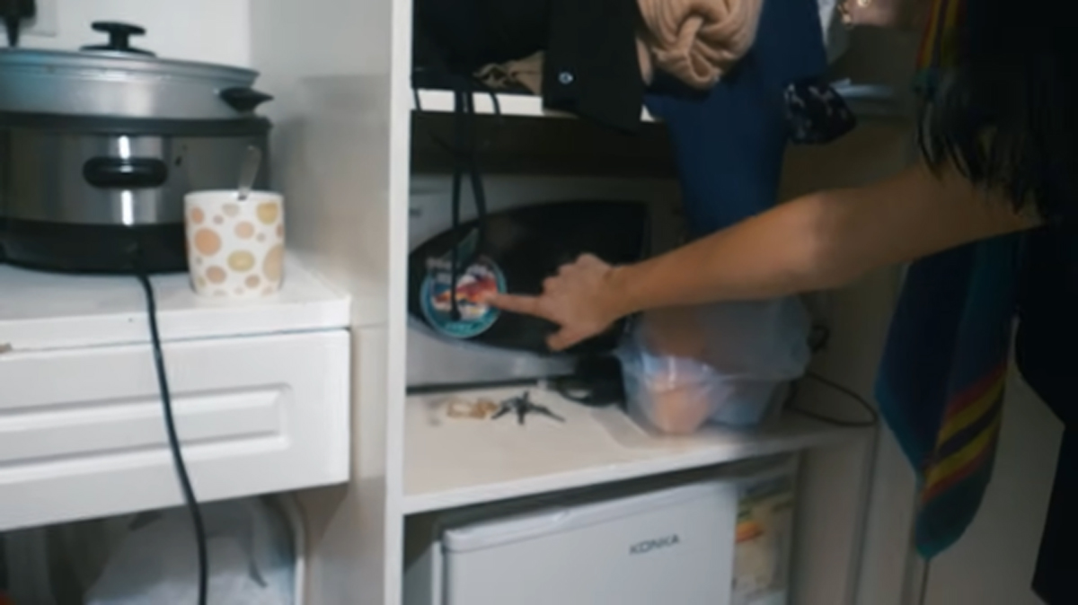 Otevřené police se spotřebiči a oblečením v malém bytě.