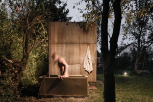 Venkovní vana u sauny vyrobené z europalet a sklolaminátu, umístěná v městské zahradě pod ovocnými stromy.
