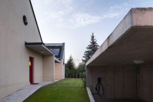 Vstupní část domu s červenými dveřmi a garáží s nabíjecí stanicí u rodinného domu v Křenovicích.