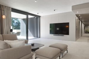 Obývací pokoj s integrovanou TV stěnou a velkoformátovým oknem do zeleně.