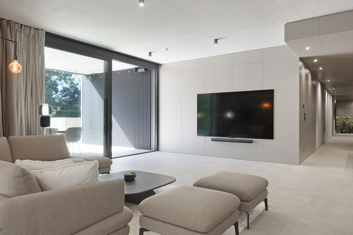 Obývací pokoj s integrovanou TV stěnou a velkoformátovým oknem do zeleně.