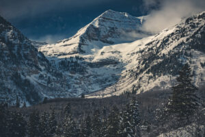Zasněžené hory Mount Timpanogos s hustými jehličnany a dramatickou oblohou.