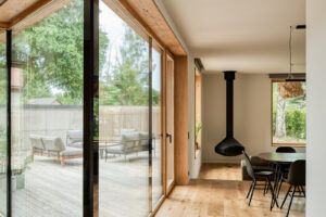 Prosklený roh domu s dřevěným rámem a výhledem na terasu.