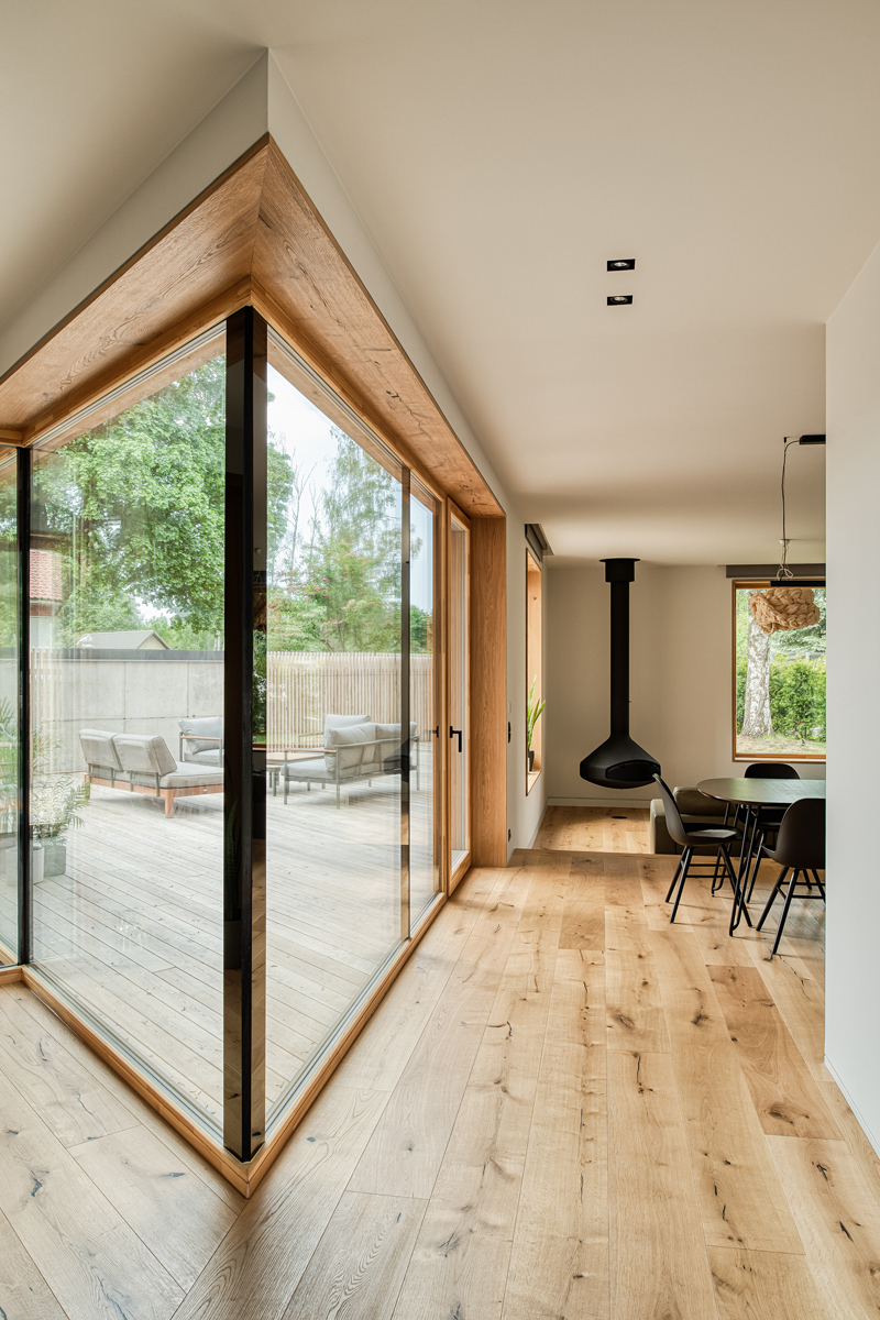 Prosklený roh domu s dřevěným rámem a výhledem na terasu.