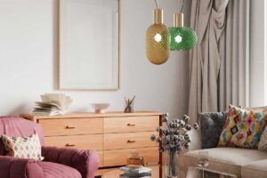 Obývací pokoj s růžovým křeslem a polštáři s pestrými vzory, doplněný skleněnými závěsnými lampami.