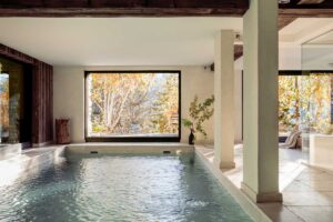 Původní hotelový bazén zasazený do prostoru s přírodními materiály a výhledem na stromy.