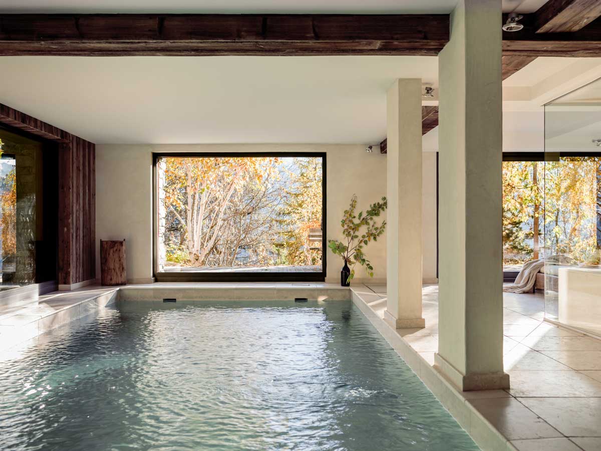 Původní hotelový bazén zasazený do prostoru s přírodními materiály a výhledem na stromy.