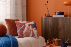 Moderní obývací pokoj s oranžovou stěnou doplněný burgundy prvky pro harmonické a výrazné barevné sladění.