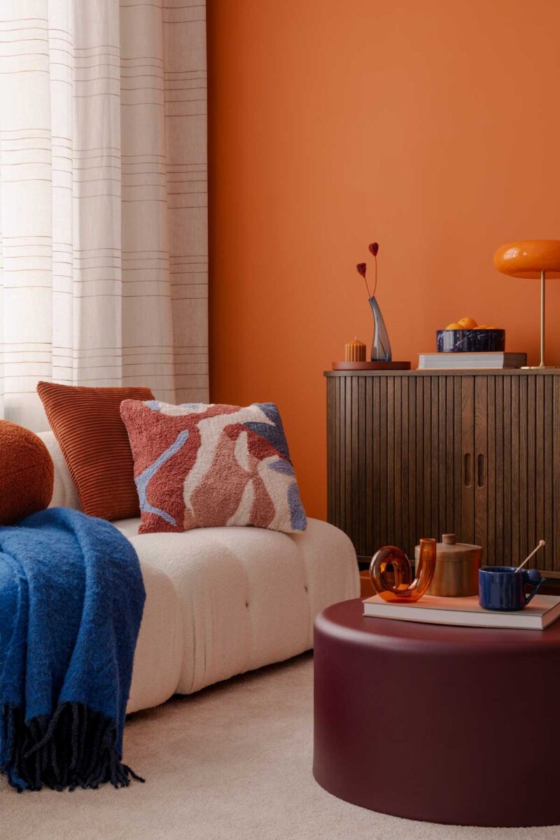 Moderní obývací pokoj s oranžovou stěnou doplněný burgundy prvky pro harmonické a výrazné barevné sladění.
