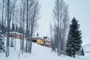 Osvětlená chata v zimním lese při soumraku.