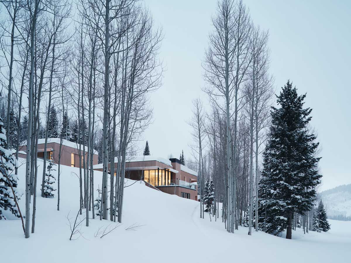 Osvětlená chata v zimním lese při soumraku.