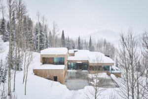 Letecký snímek horské chaty obklopené zasněženými stromy.