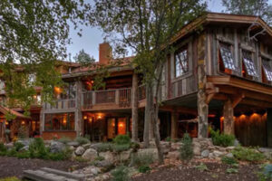 Rustikální dřevěná budova s prosklenými okny a teplým osvětlením zasazená mezi stromy.