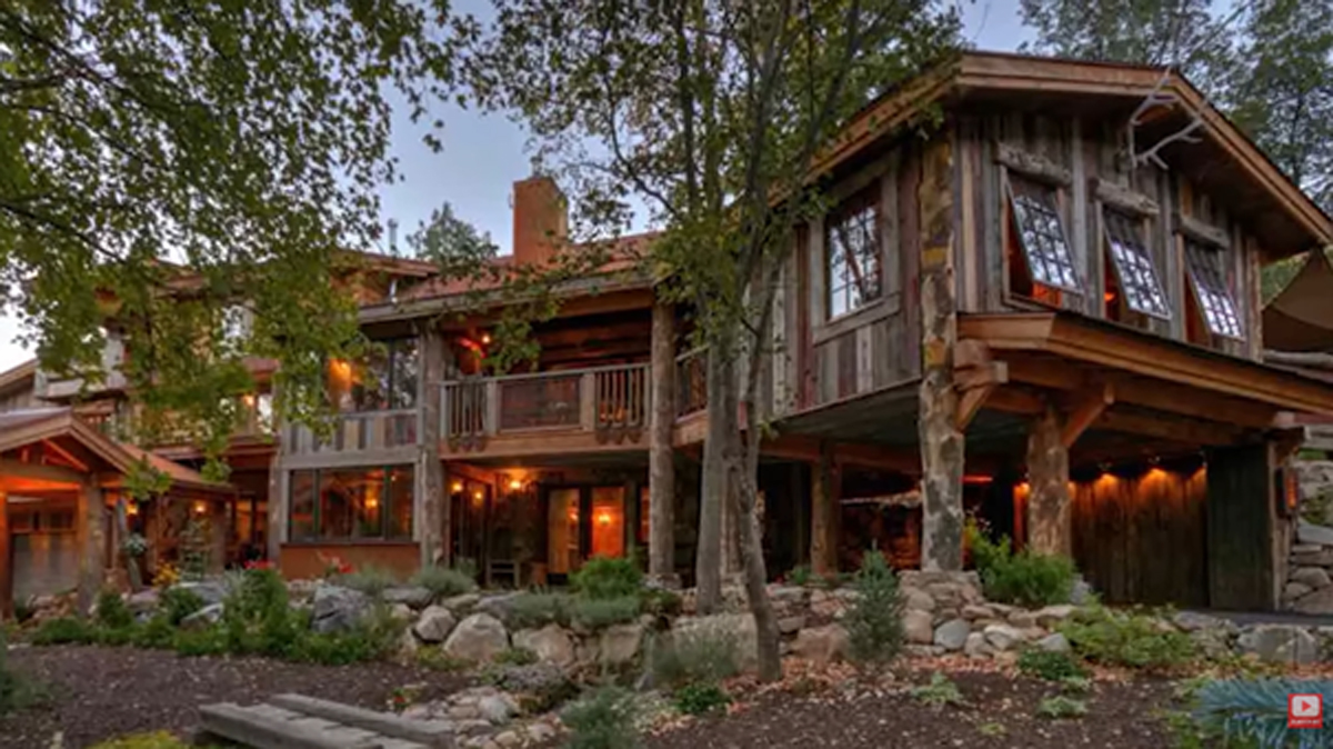 Rustikální dřevěná budova s prosklenými okny a teplým osvětlením zasazená mezi stromy.