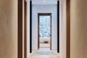Minimalistická chodba s dřevěnou podlahou a výhledem na zasněžený les.