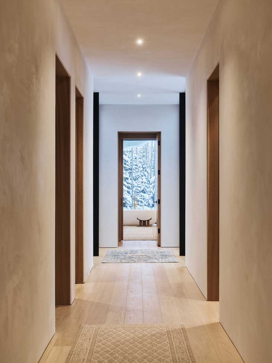 Minimalistická chodba s dřevěnou podlahou a výhledem na zasněžený les.