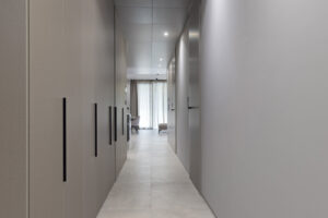 Úzká chodba se zapuštěnými dveřmi a minimalistickým osvětlením v jednotné paletě šedých tónů.