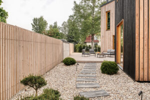 Cesta z kamenných dlaždic mezi okrasnými keři a štěrkovým záhonem vedoucí k terase domu.