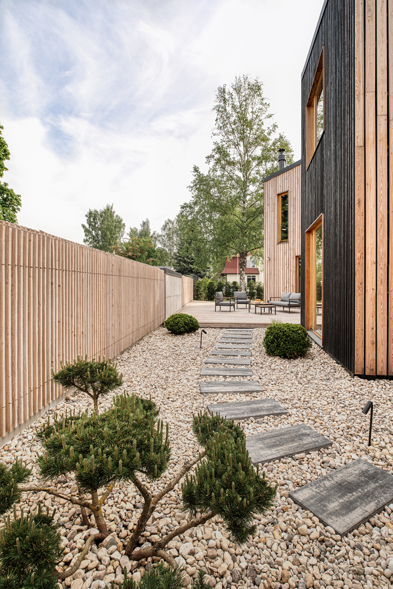 Cesta z kamenných dlaždic mezi okrasnými keři a štěrkovým záhonem vedoucí k terase domu.