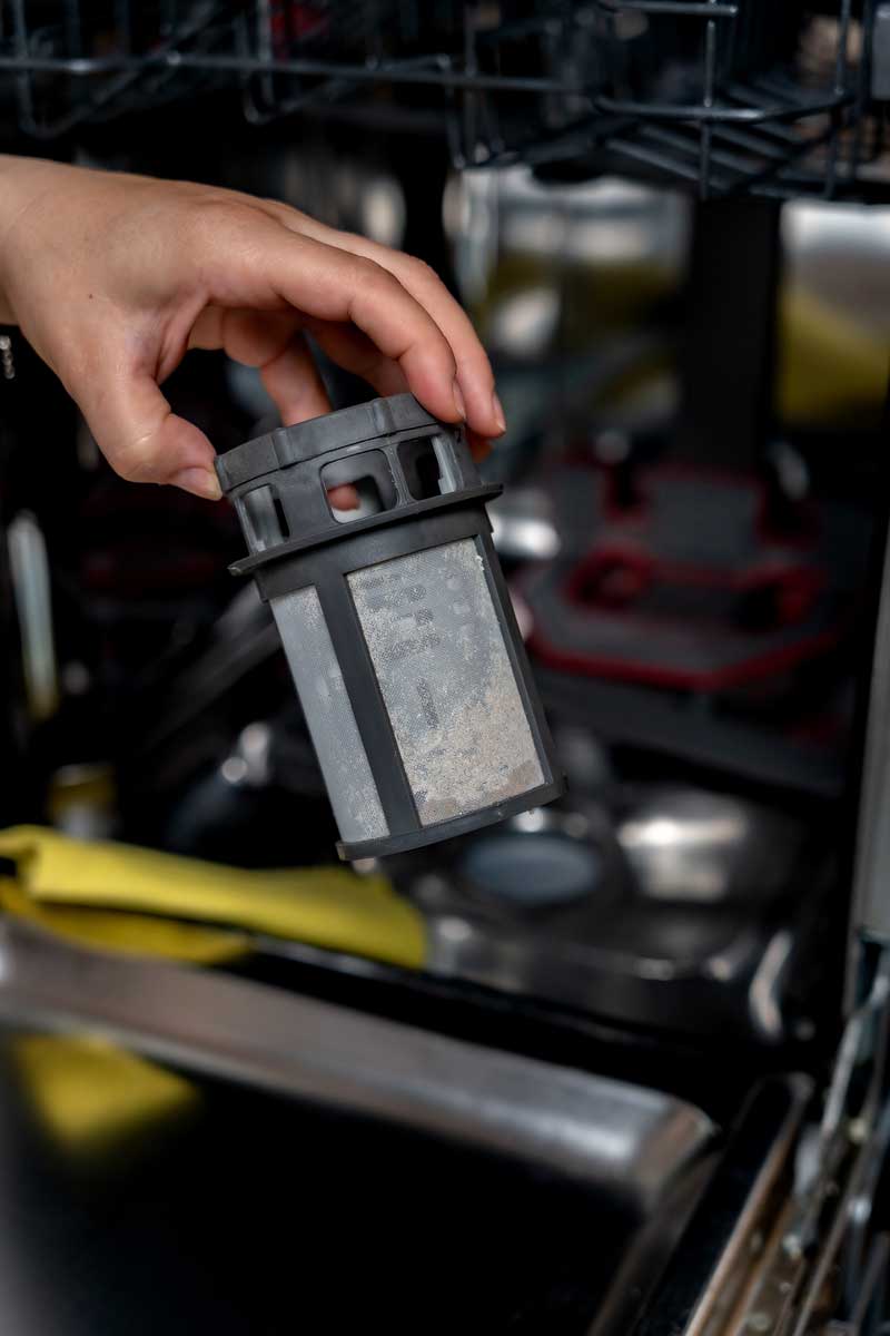 Ruka drží vyjmutý filtr z myčky určený k pravidelnému čištění.