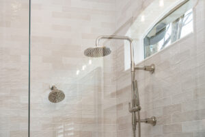 Čistý sprchový kout s prosklenou stěnou, nerezovým sprchovým setem a světlými obklady.