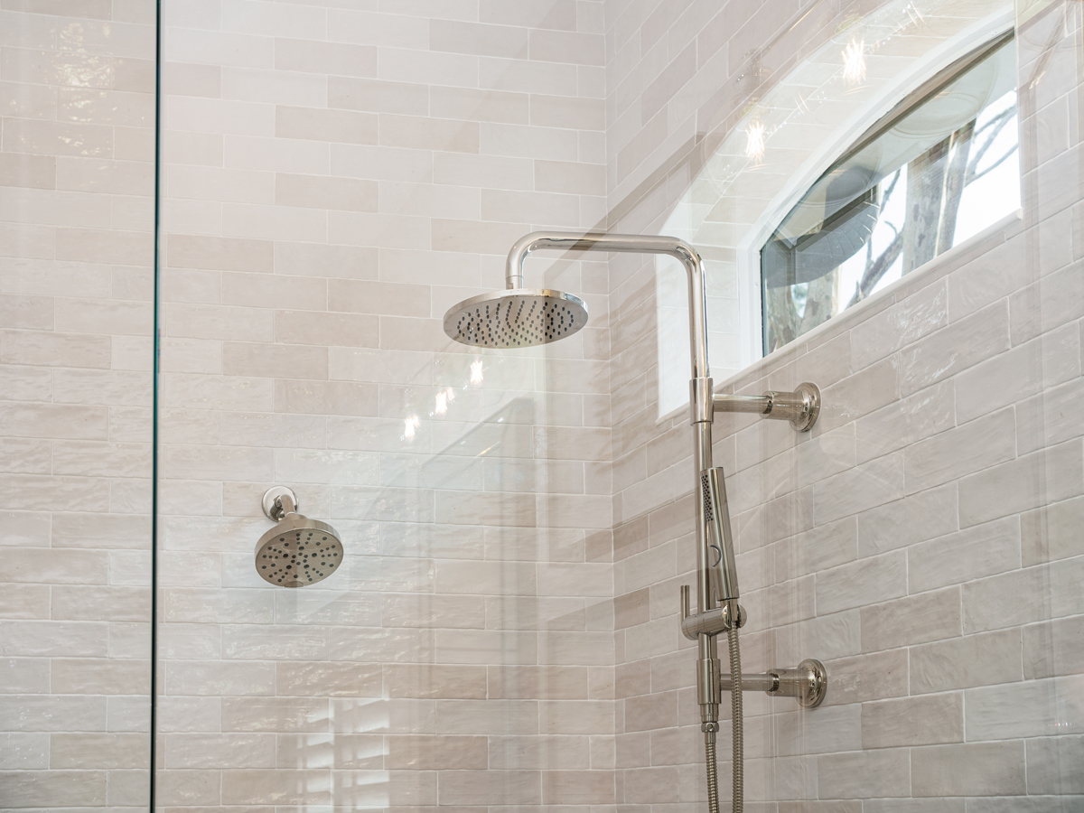 Čistý sprchový kout s prosklenou stěnou, nerezovým sprchovým setem a světlými obklady.