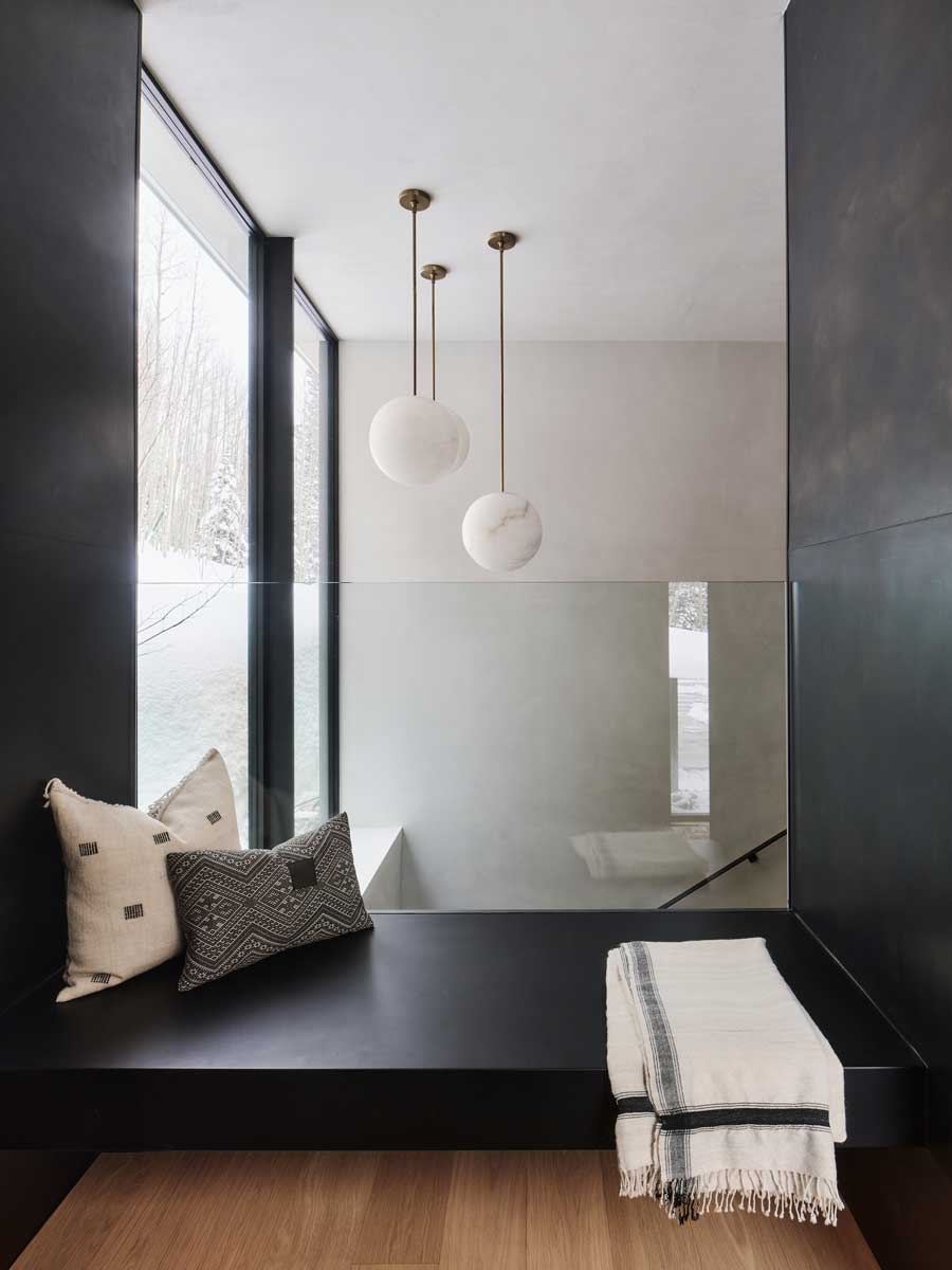 Pohodlný čtecí koutek s polštáři a dekou u okna.