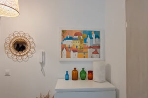 Předsíň s bílou komodou, barevnými vázami a obrazem v teplých odstínech.