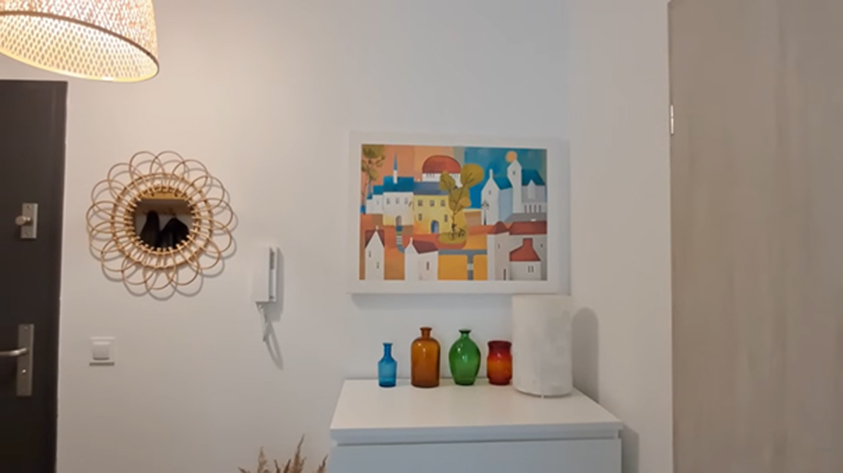 Předsíň s bílou komodou, barevnými vázami a obrazem v teplých odstínech.