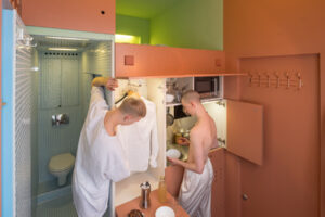 Multifunkční prostor mikrobytu s kuchyňským koutem, sprchou a výrazným barevným řešením.