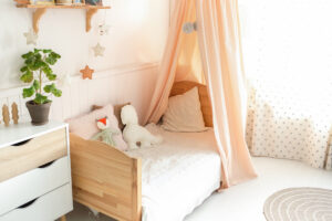 Dětská postýlka s baldachýnem z jemné látky, polštáři a plyšovými hračkami v měkkých barvách.