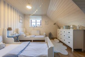 Dětský pokoj pro dvě děti s bílým nábytkem, dřevěnou podlahou a klidnými neutrálními barvami.