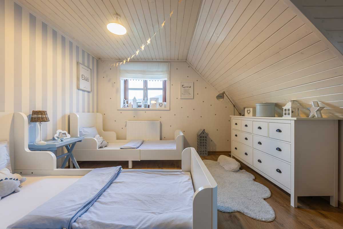 Dětský pokoj pro dvě děti s bílým nábytkem, dřevěnou podlahou a klidnými neutrálními barvami.