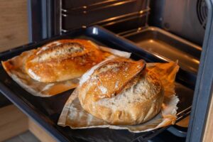 Dva bochníky domácího chleba pečené z kynutého těsta v troubě na pečicím papíře.