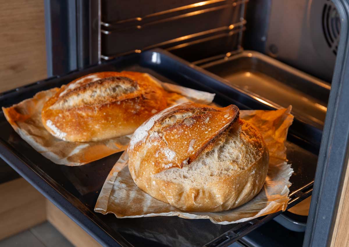 Dva bochníky domácího chleba pečené z kynutého těsta v troubě na pečicím papíře.