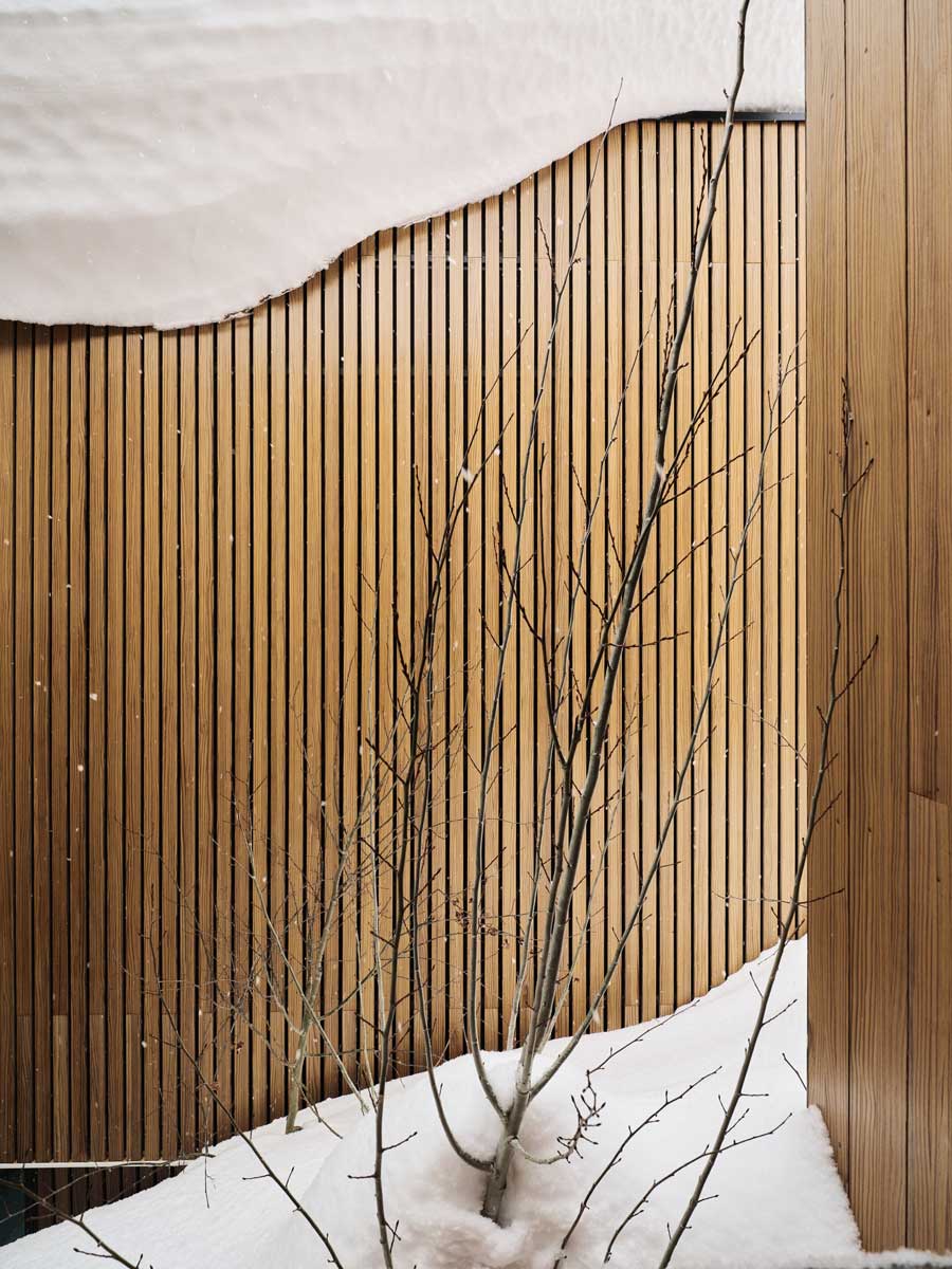 Detail svislé dřevěné fasády částečně pokryté sněhem.