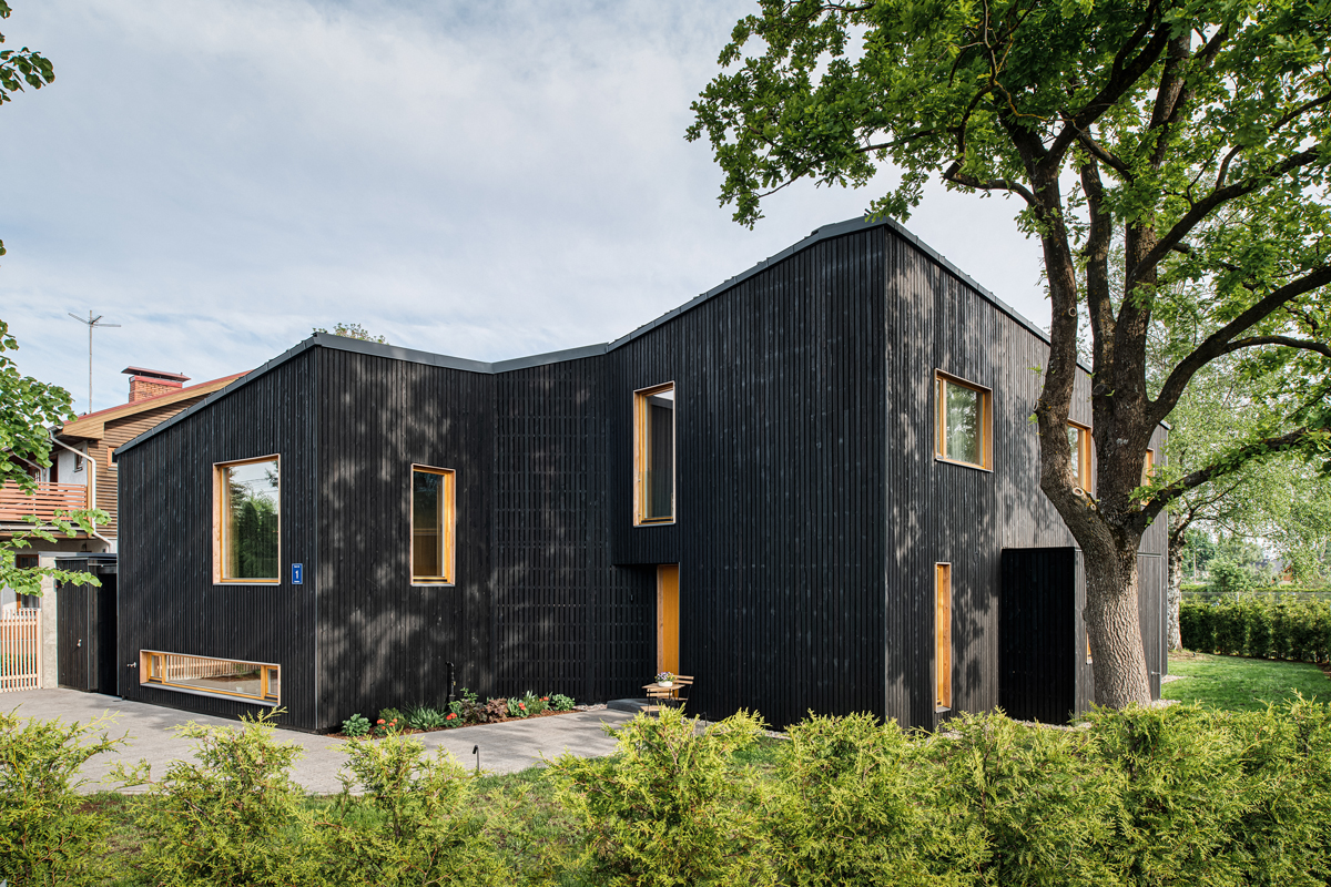 Exteriér moderního domu s černě opalovaným dřevěným obkladem a nepravidelnými okny.