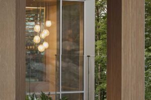 Prosklená chodba s masivními sloupy propojuje části domu a nechává interiér dýchat spolu s okolní krajinou