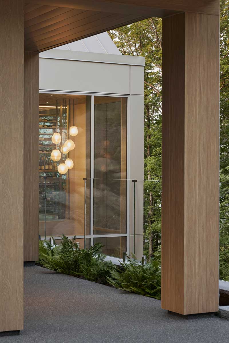 Prosklená chodba s masivními sloupy propojuje části domu a nechává interiér dýchat spolu s okolní krajinou