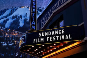 Noční pohled na budovu kina s nápisem Sundance Film Festival a zasněženým horským pozadím.