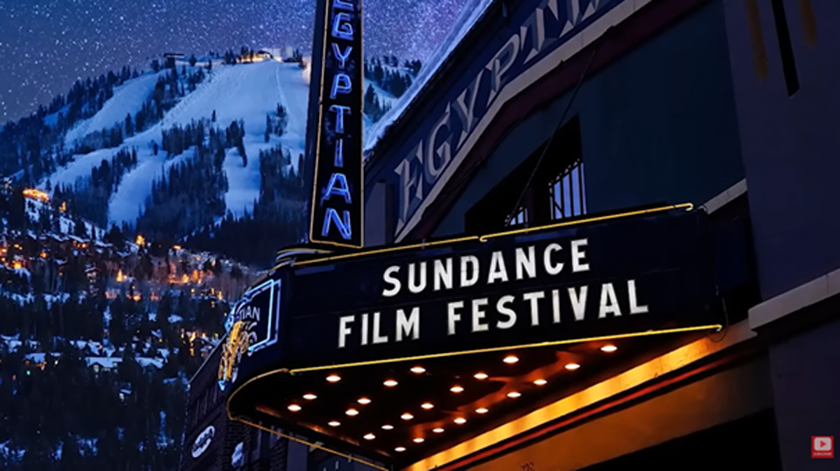 Noční pohled na budovu kina s nápisem Sundance Film Festival a zasněženým horským pozadím.