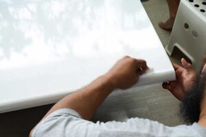 Aplikace nové bílé samolepicí fólie na nábytkovou desku.