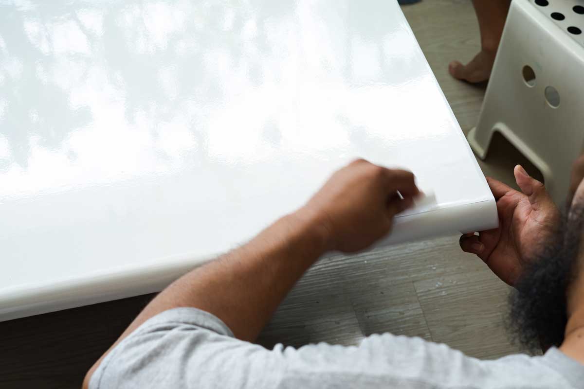 Aplikace nové bílé samolepicí fólie na nábytkovou desku.