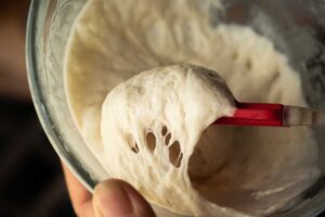 Detail na pružné kynuté těsto nabrané silikonovou stěrkou z mísy.